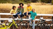 Group of friends sit on fence near several Electra electric bicycle models Group of friends sit on fence near several Electra electric bicycle models